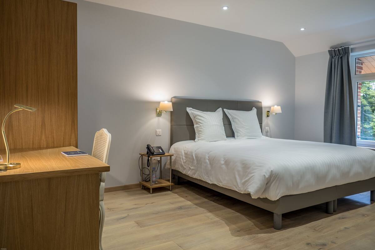 Une chambre moderne avec un bureau en bois, un lit avec une literie blanche et deux lampes fixées au mur.