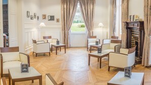 A hotel lobby with a wooden floor, several armchairs, a fireplace, and framed pictures on the wall. - Hôtel Château de la Marlière (Fourmies)