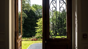 A doorway with a wooden door and a metal gate, leading to a garden with a paved path. - Hôtel Château de la Marlière (Fourmies)