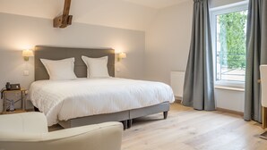 A modern bedroom with a large bed, bedside lamps, a wooden accent wall, and a view through a window with curtains. - Hôtel Château de la Marlière (Fourmies)