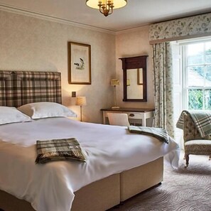 A hotel room with a large bed, a desk, a chair, a mirror, and a window with curtains.