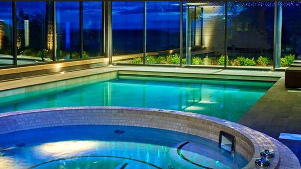 Zwembad met een hottub in het midden, omringd door ligbedden en uitzicht op de stad 's nachts.