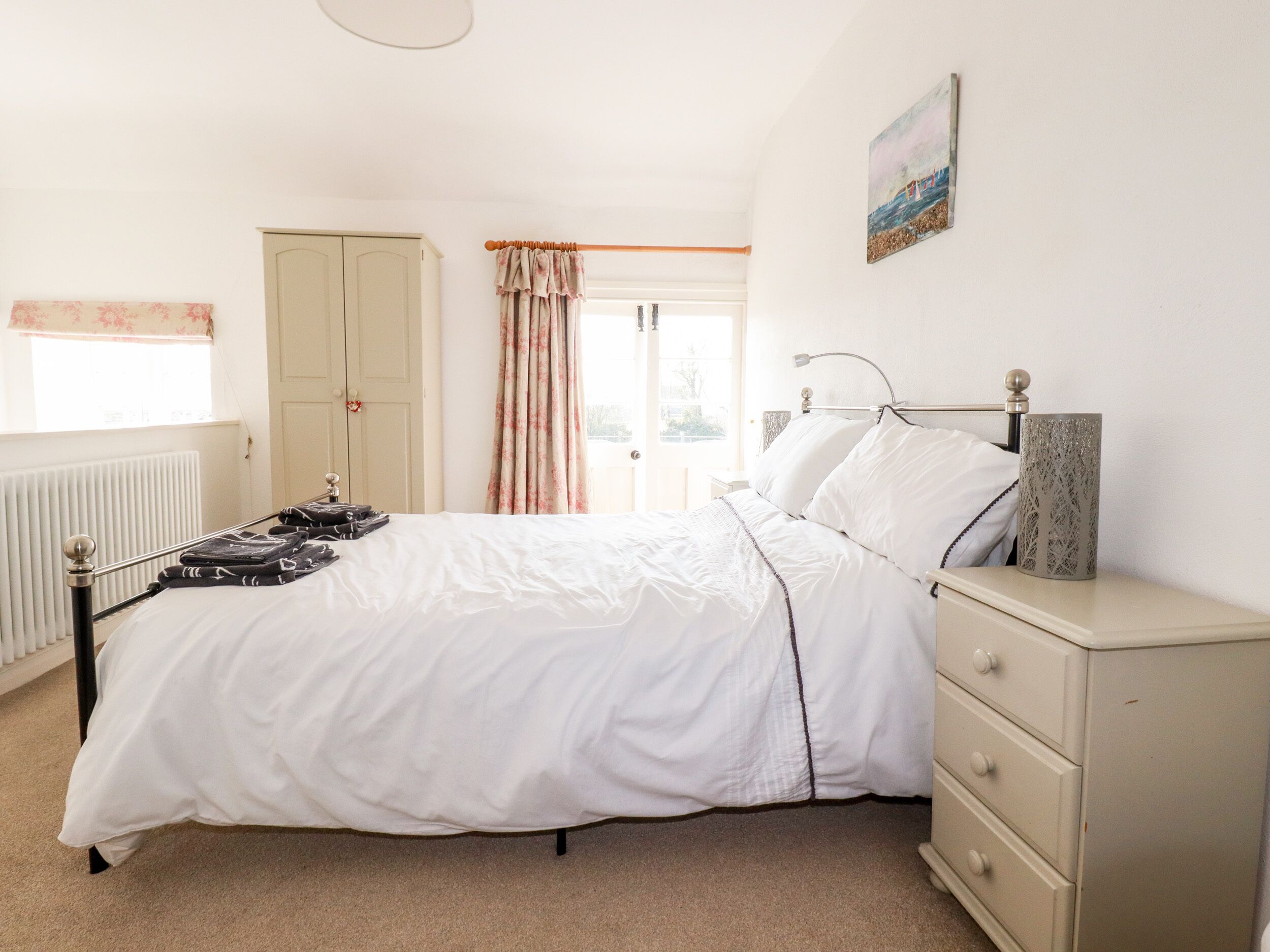 A bedroom with a bed, a dresser, a radiator, a window with curtains, and a door.
