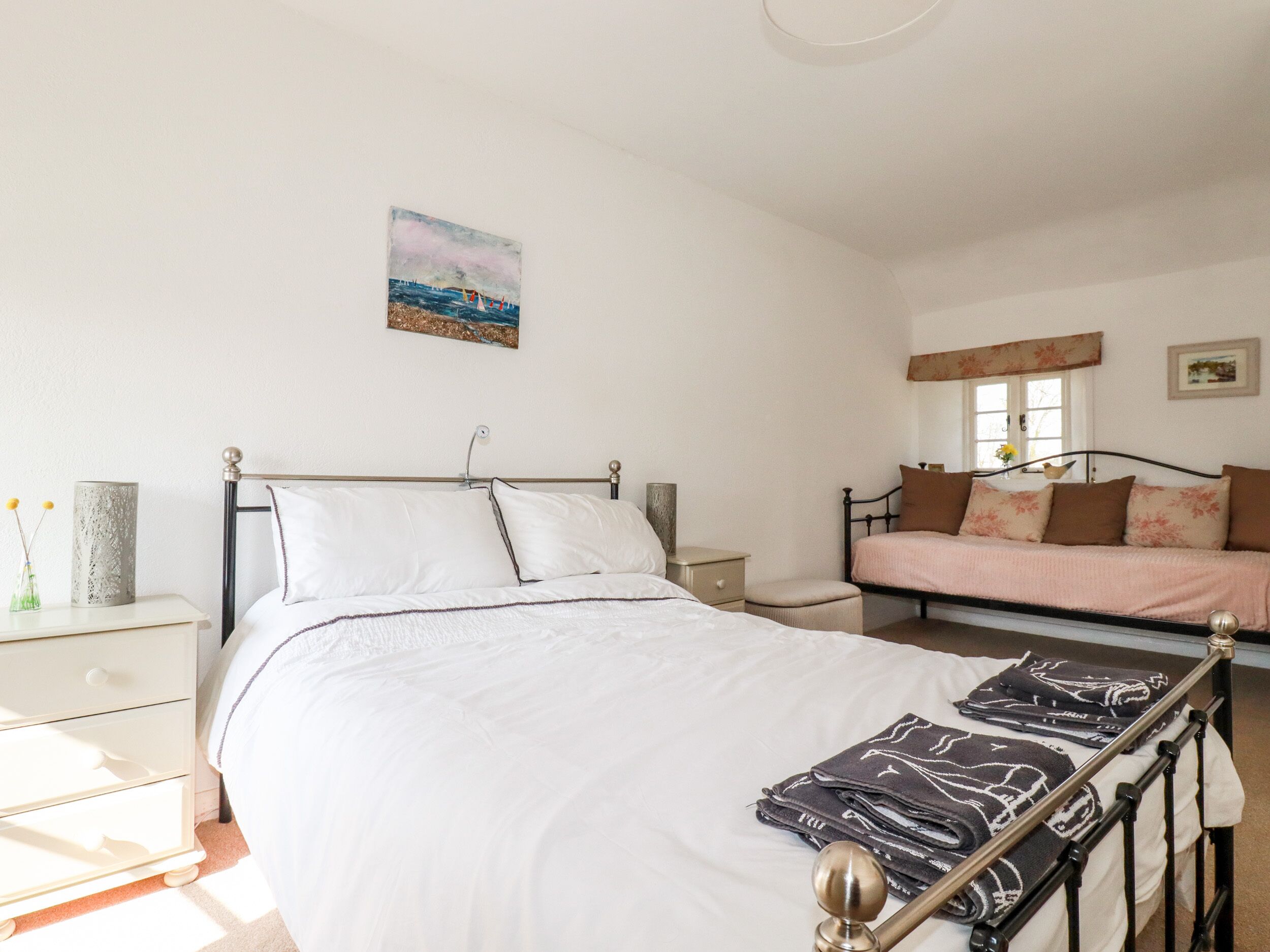 A bedroom with a bed, bedside tables, a nightstand, a sofa, and a window.