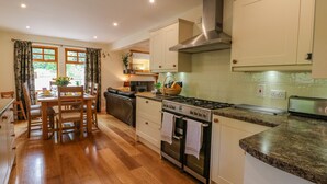 A modern kitchen with wooden flooring, a gas stove, stainless steel appliances, and a dining area with a table and chairs. - Thistle Dhu (Newtonmore)