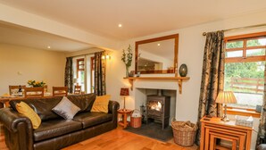 A cozy living room with a fireplace, wooden furniture, and a dining area. - Thistle Dhu (Newtonmore)