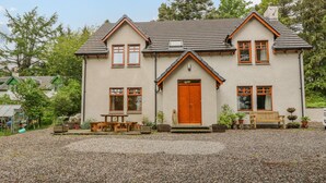 A two-story house with a gravel driveway, wooden bench, and potted plants. - Thistle Dhu (Newtonmore)