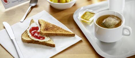 Un plateau de petit-déjeuner avec des toasts, de la confiture, du thé et un bol de fruits.