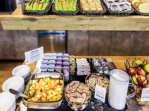 Ein Buffet mit verschiedenen Speisen, darunter Obst, Joghurts und verpackten Snacks.