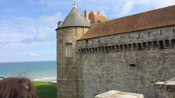 Un edificio histórico de piedra con una torre y vistas al mar.