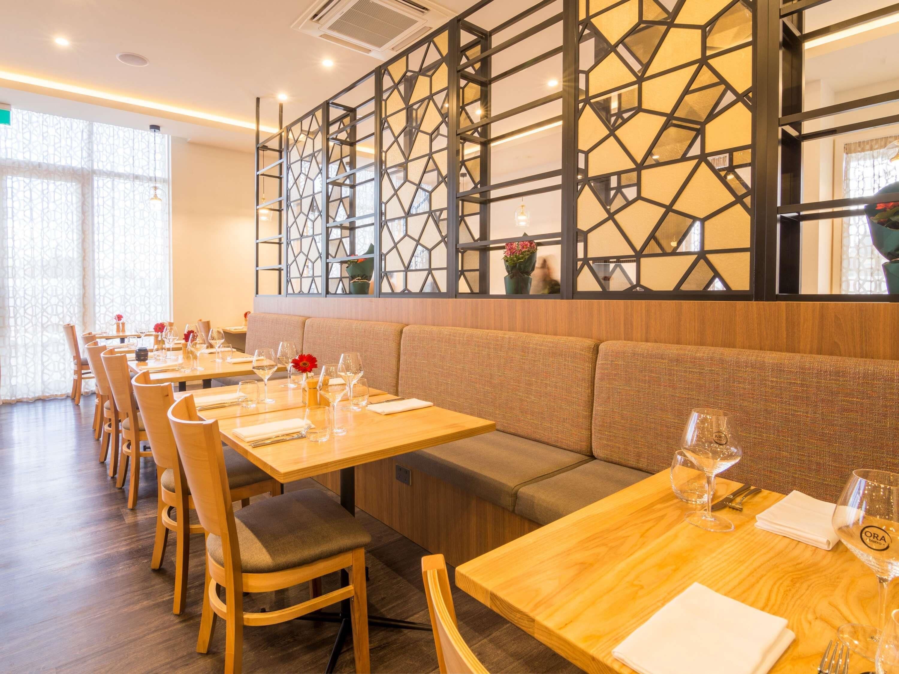 Interior de restaurante con mesas de madera, asientos acolchados y un separador decorativo.