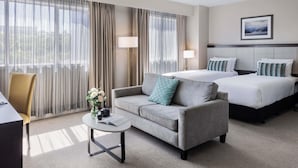 A hotel room with a sofa, two beds, a small table with a book, and a lamp.