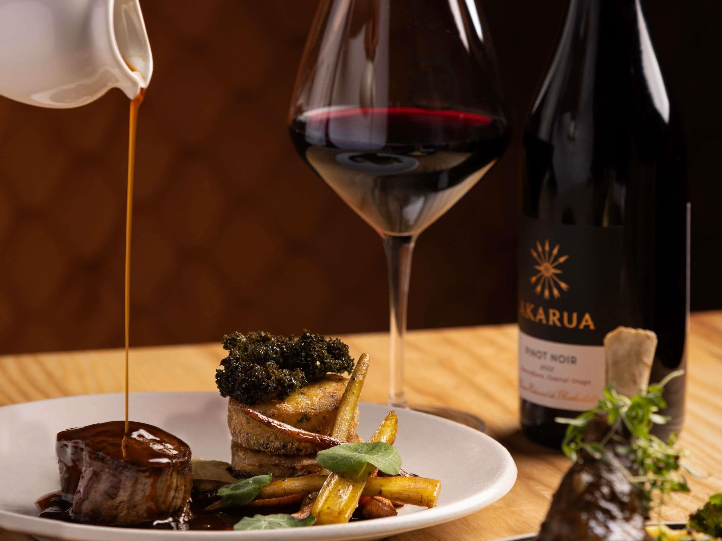 A plate of food with a bottle of wine and a glass of red wine.