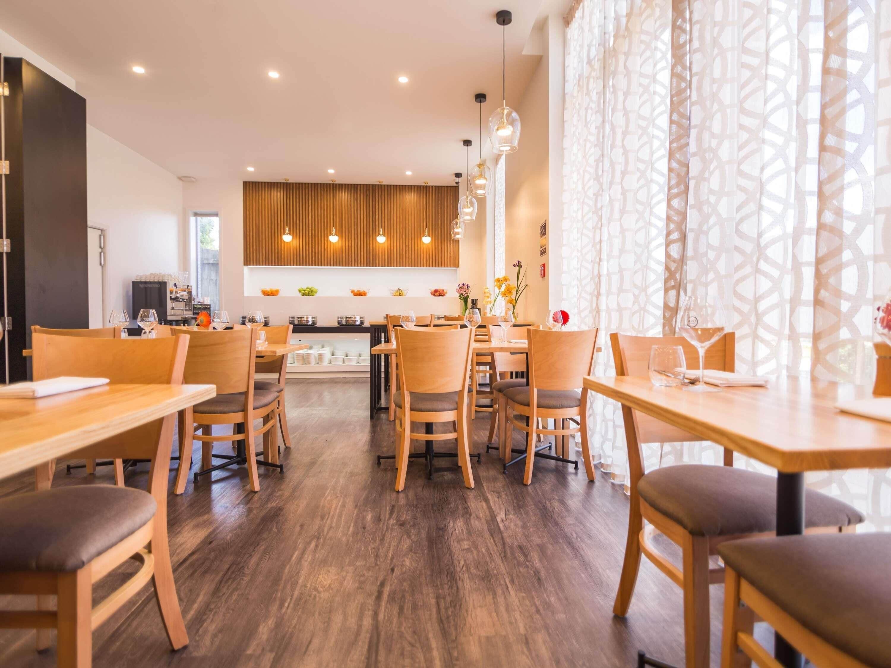 Ein modernes Restaurant mit Holztischen, Pendelleuchten und einer zentralen Küchenzeile.
