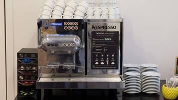 A Nespresso coffee machine with multiple coffee cups stacked above it, a coffee pod dispenser, and a stack of plates and cups on the counter.