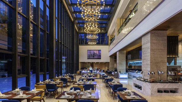 Un vaste espace de restauration d’hôtel, doté de nombreuses tables et chaises, d’un grand lustre et d’un aménagement intérieur moderne.