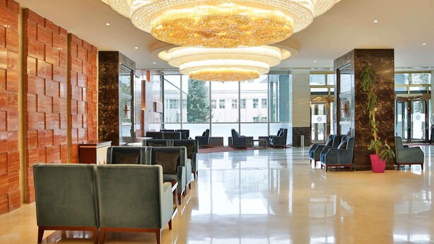 A spacious lobby with a large chandelier, seating area, and large windows offering a view of the city. - Novotel Ulaanbaatar (Ulaanbaatar)