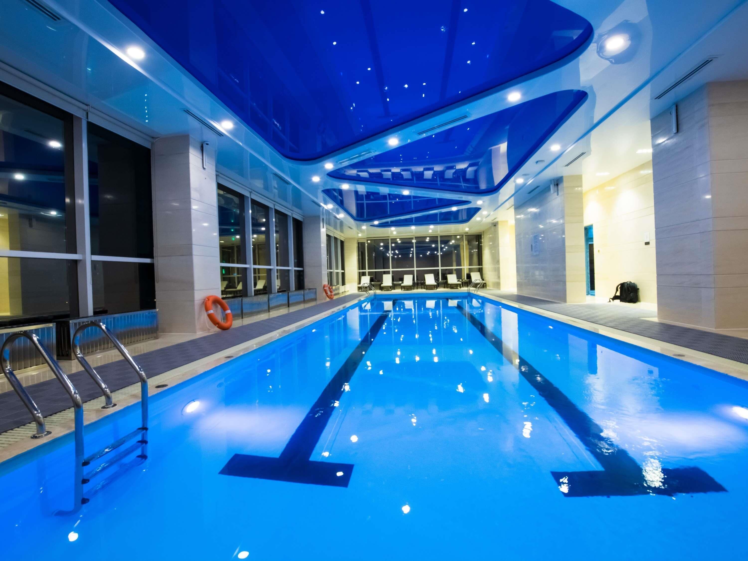 Une piscine intérieure à l’eau claire, dotée d’échelles en métal et de chaises longues disposées le long des murs.