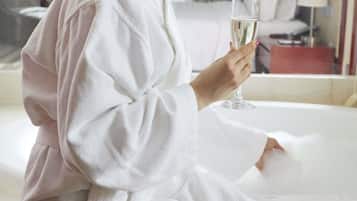 Une personne vêtue d’un peignoir blanc est assise dans une baignoire, un verre de champagne à la main.