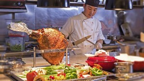 A chef carving a large roasted bird in a commercial kitchen with various vegetables and cooking utensils on the counter. - Novotel Ulaanbaatar (Ulaanbaatar)