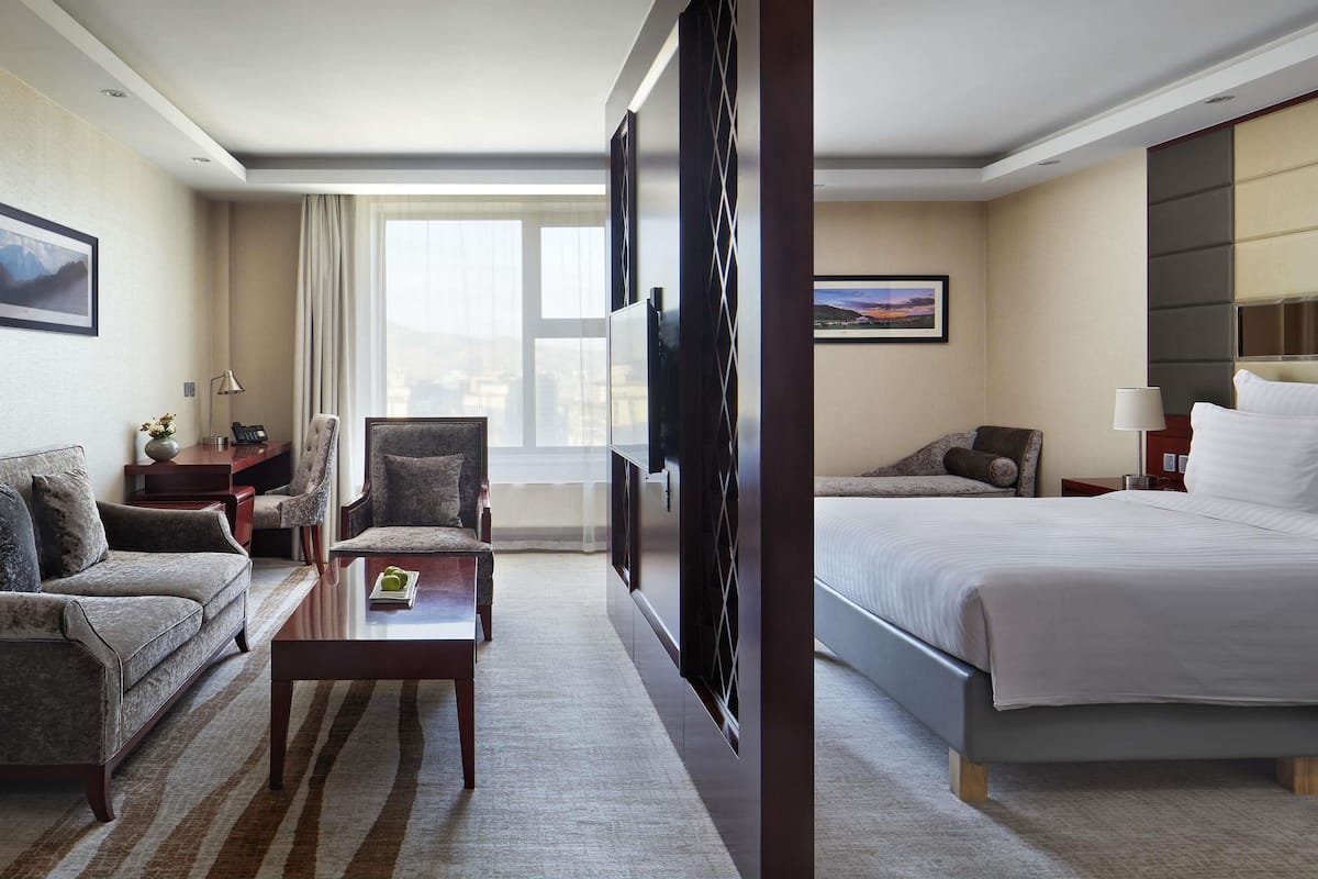 Una habitación de hotel con cama, sofá, escritorio con lámpara, silla, televisor y ventana con vistas.