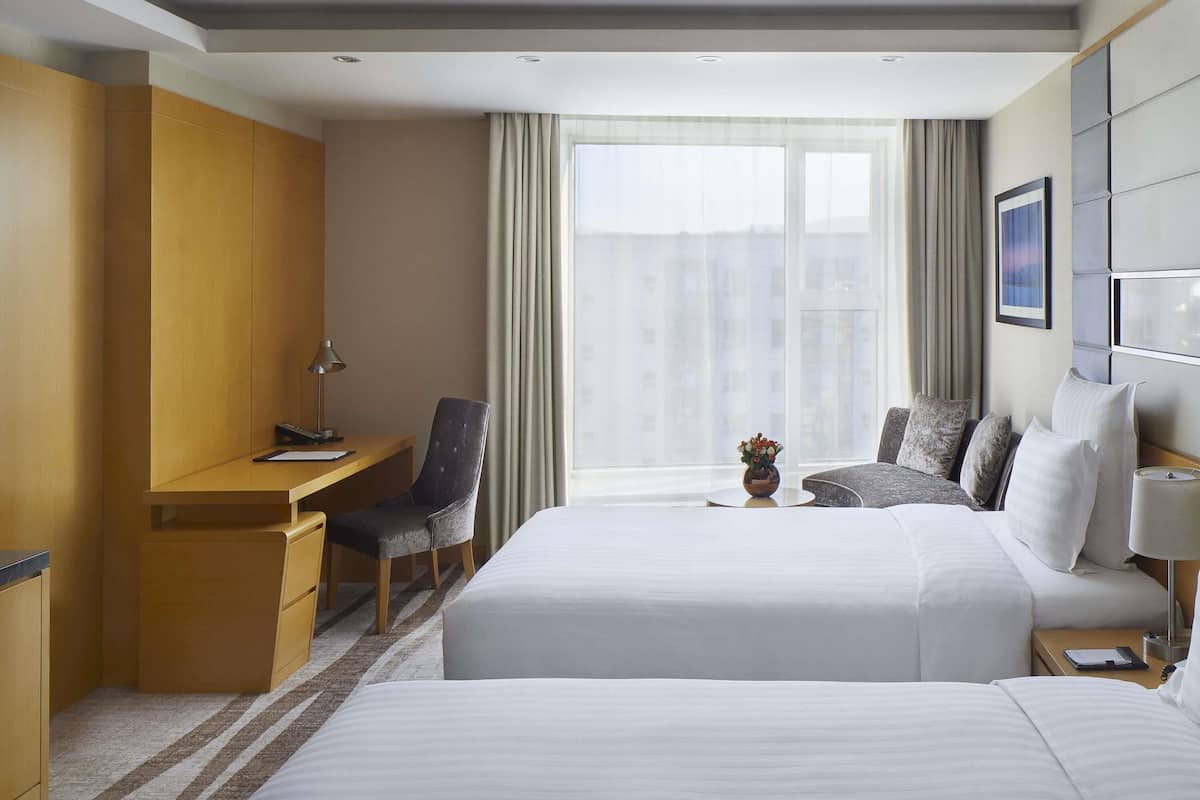 Habitación de hotel con cama, escritorio, silla y un amplio ventanal con cortinas.
