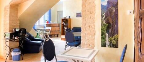 A cozy living area with a stone archway, a dining table, blue chairs, a sofa, and a bookshelf.