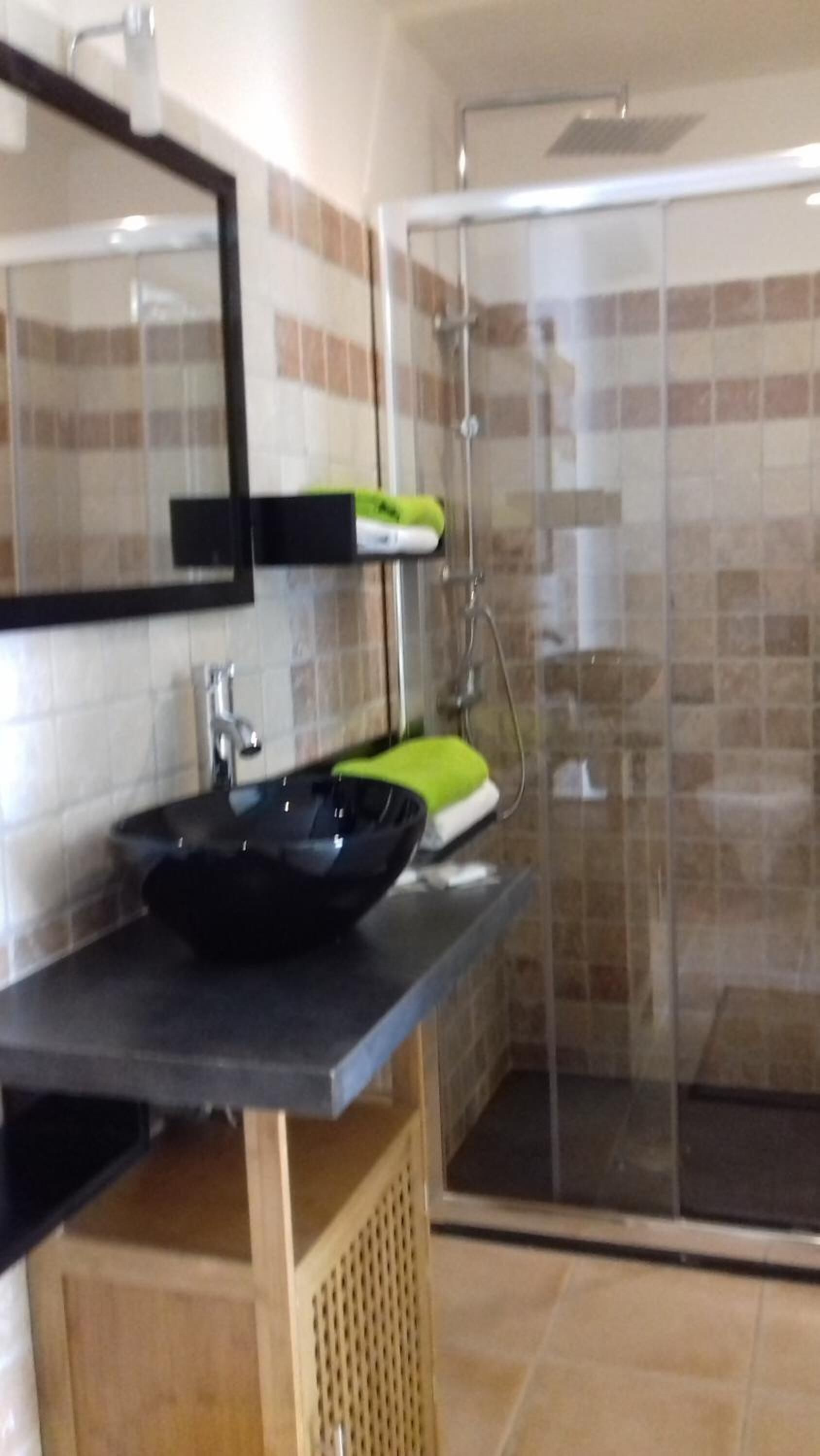 Un baño con un lavamanos negro, un espejo y un box de ducha.