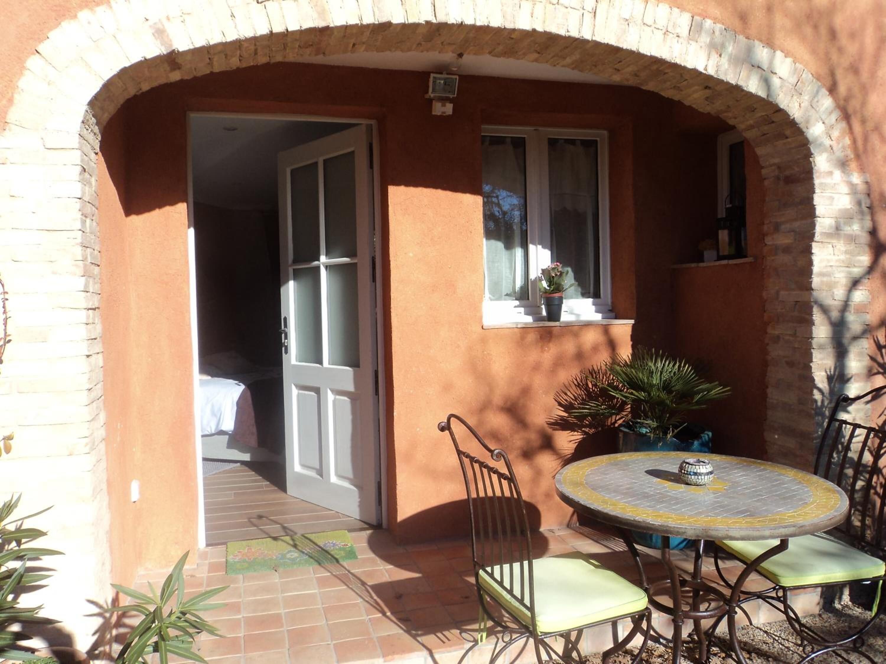 Un patio al aire libre con una mesa redonda y sillas, una planta en maceta y una puerta que da a una habitación.