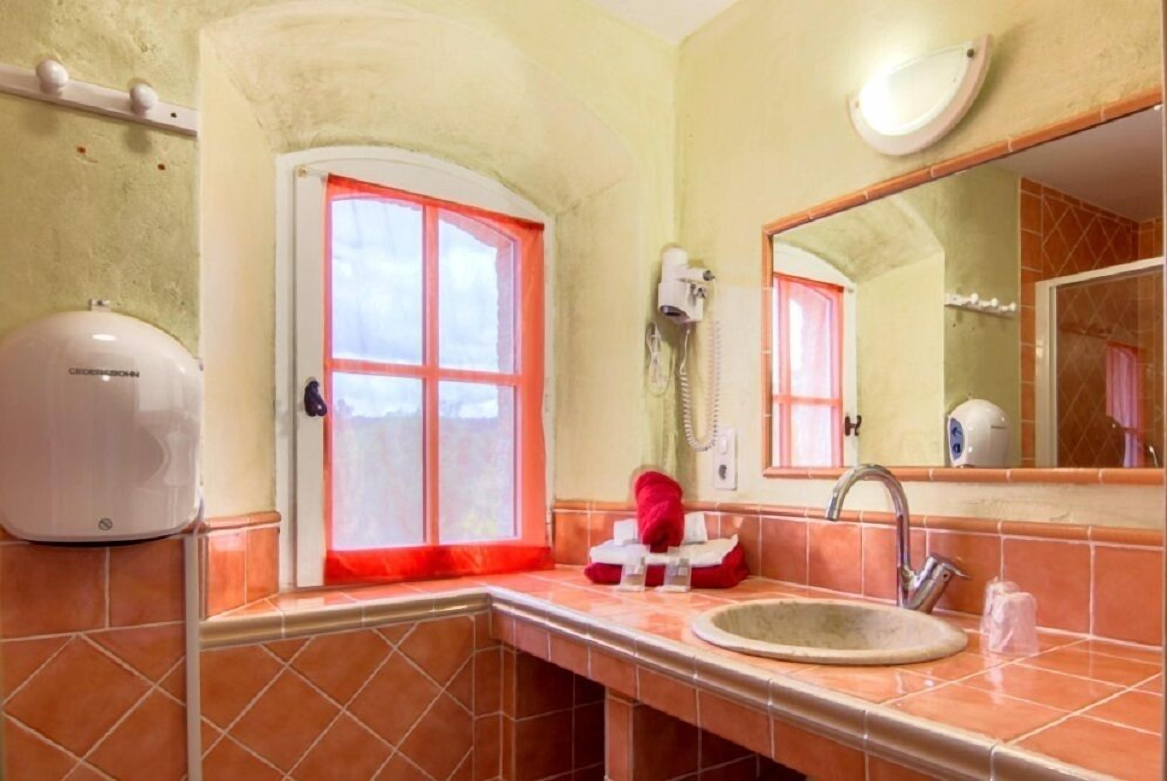 Een badkamer met een wastafel, spiegel en een aan de muur bevestigde haardroger.