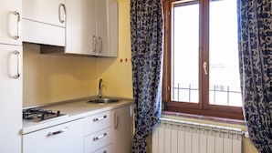 A compact kitchen with white cabinets, a stainless steel sink, and a window with patterned curtains. - Residence Massa Alta (Massa Marittima)