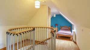 A bedroom with a wooden bed, a blue accent wall, and a staircase with a wooden handrail. - Kamba Cottage (Forfar)