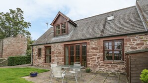 A stone house with a tiled patio, a dining table, and chairs. - Kamba Cottage (Forfar)