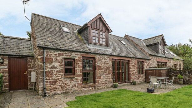 A stone house with a tiled roof, a wooden door, and a patio with outdoor furniture. - Kamba Cottage (Forfar)