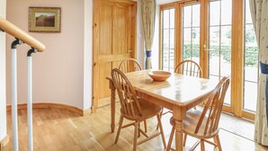 A dining area with a wooden table and chairs, a wooden door, and a window with curtains. - Kamba Cottage (Forfar)