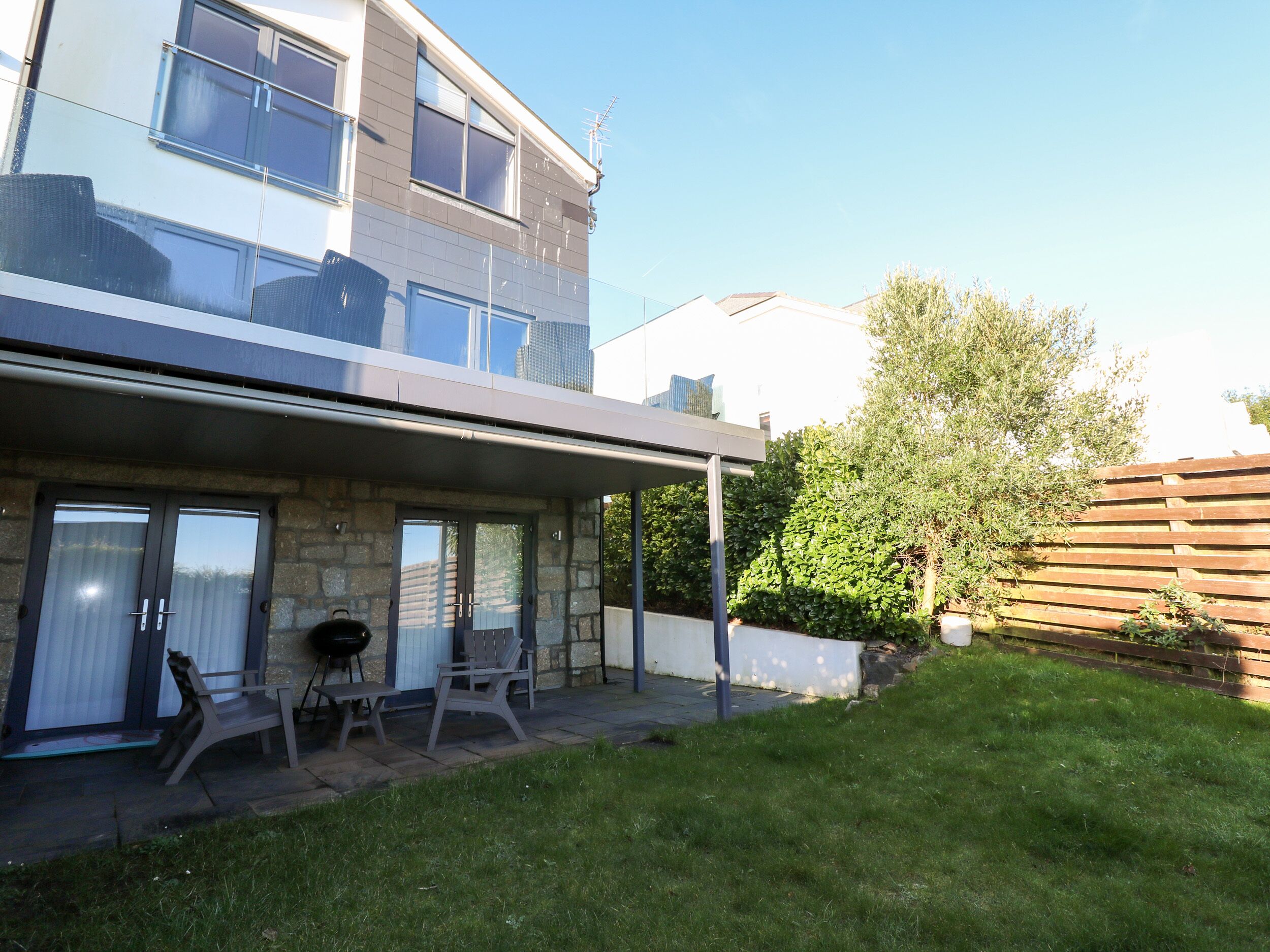 A modern house with a covered patio, stone walls, and a well-maintained lawn.