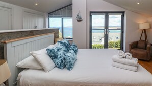 A bedroom with a large bed, a view of the sea, and a chair. - Seafield (St Ives)