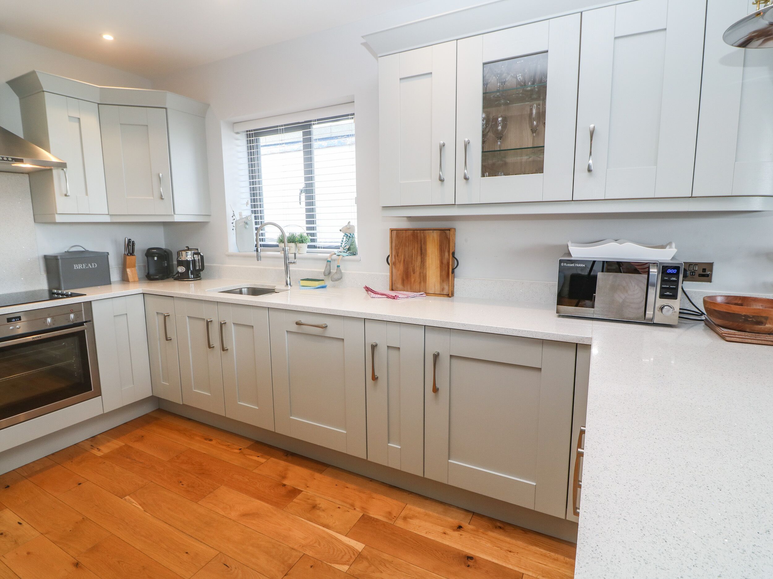 A modern kitchen with white cabinets, a built-in oven, a microwave, and a wooden countertop.