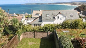 A residential property with a view of the sea, featuring a sloped roof, a fenced garden, and a brick wall. - Seafield (St Ives)