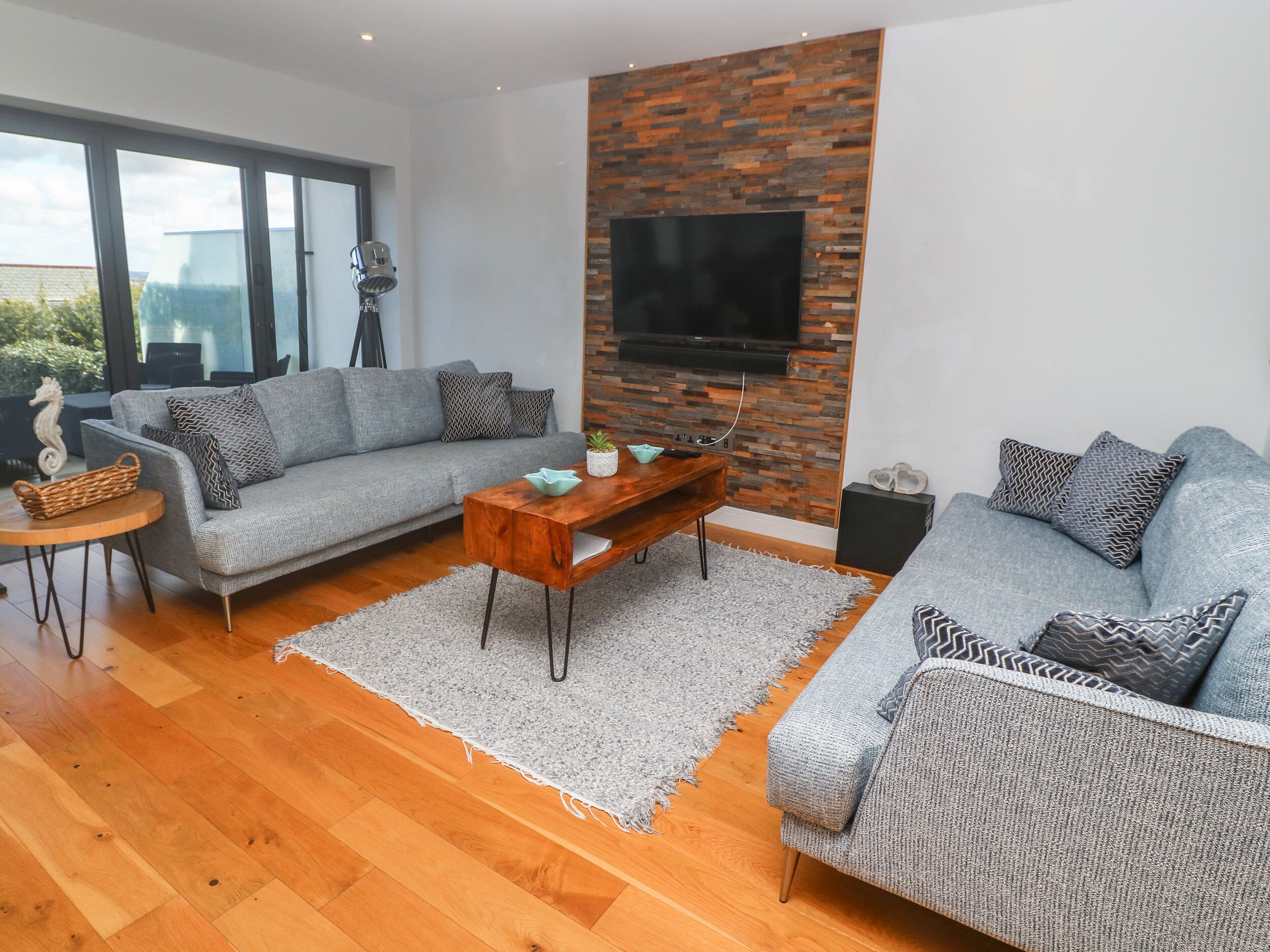 A modern living room with two grey sofas, a wooden coffee table, and a TV mounted on a brick wall.