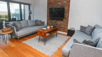 A modern living room with two grey sofas, a wooden coffee table, and a TV mounted on a brick wall.