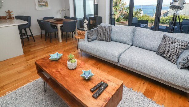 A modern living room with a grey sofa, wooden coffee table, and a dining area with a wooden table and chairs. - Seafield (St Ives)