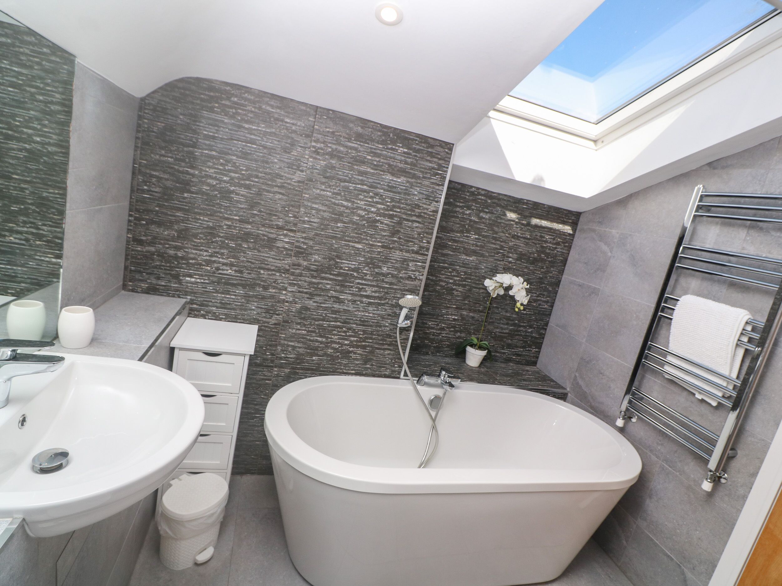 Une salle de bain moderne dotée d’une lucarne, d’une baignoire sur pieds, d’un meuble-lavabo et d’un porte-serviettes.