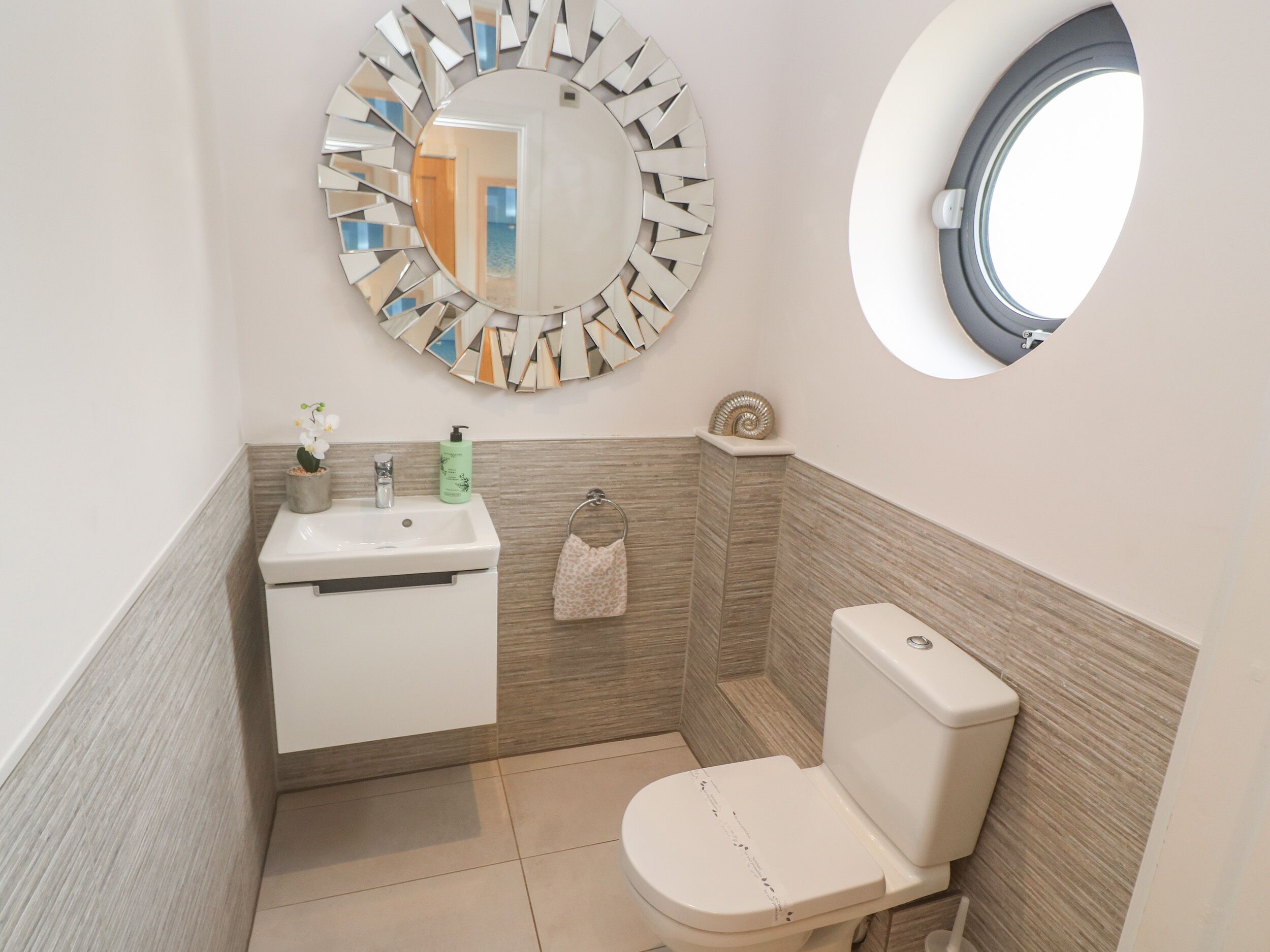 A bathroom with a round mirror, a toilet, a sink, and a small window.