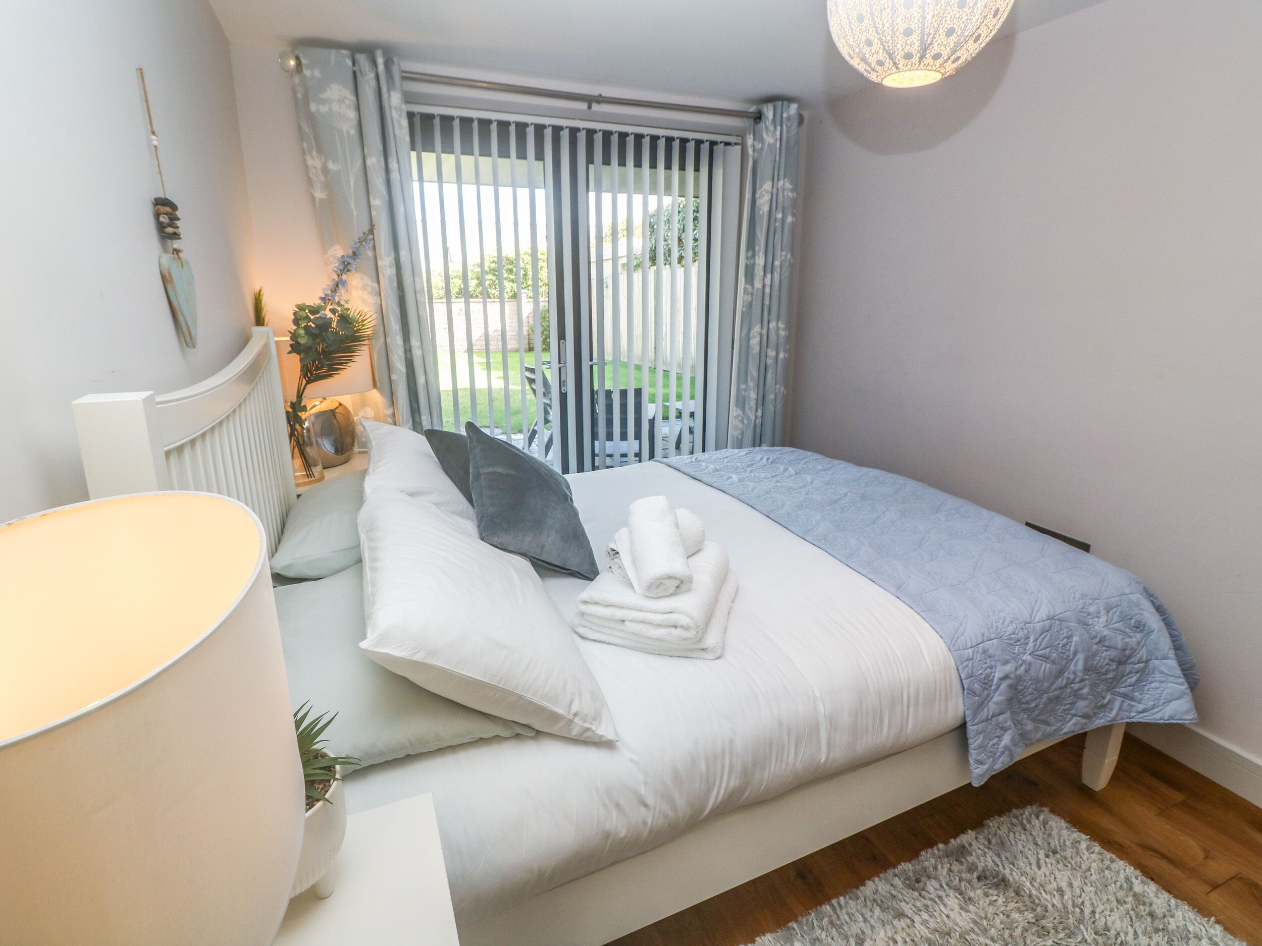 A neatly made bed with white and grey bedding, a bedside lamp, and a small potted plant.