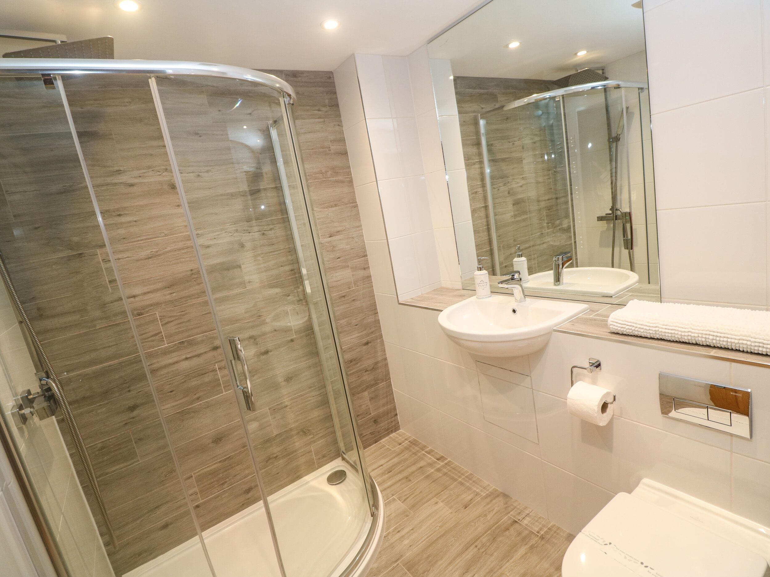 A modern bathroom with a glass-enclosed shower, a white sink, and a toilet.