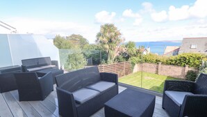 A patio with wicker furniture, a glass barrier, and a view of the sea. - Seafield (St Ives)