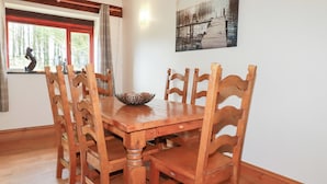 Uma área de refeições com mesa e cadeiras de madeira, uma janela com vista para árvores e um quadro na parede.