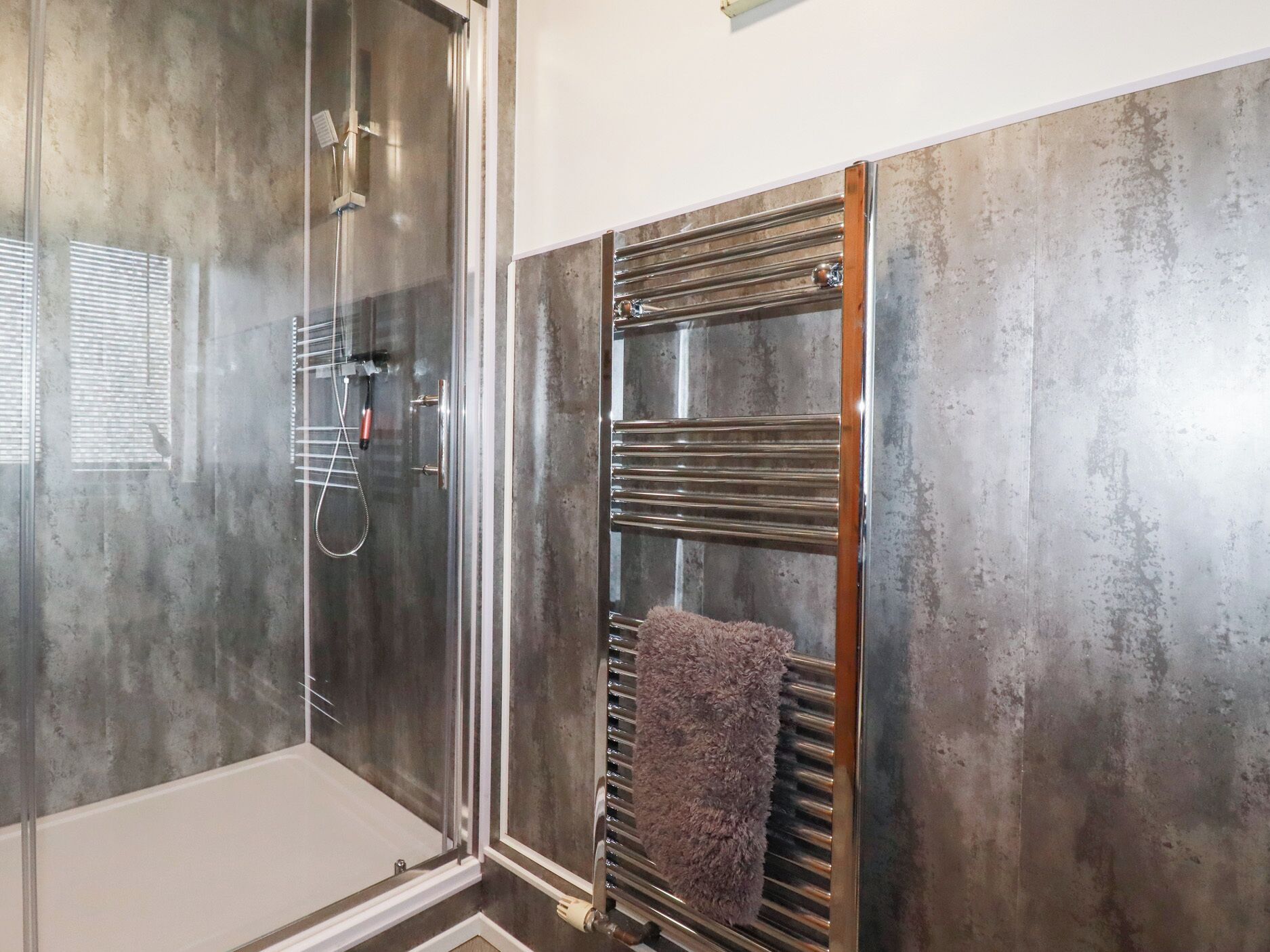 A modern bathroom with a glass shower enclosure, a built-in towel rack, and a large mirror.