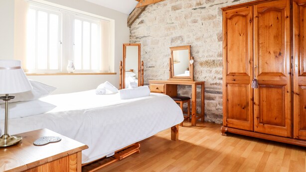 A bedroom with a bed, bedside tables, a dresser, a mirror, and a window. - Wheal Hart (Newquay)